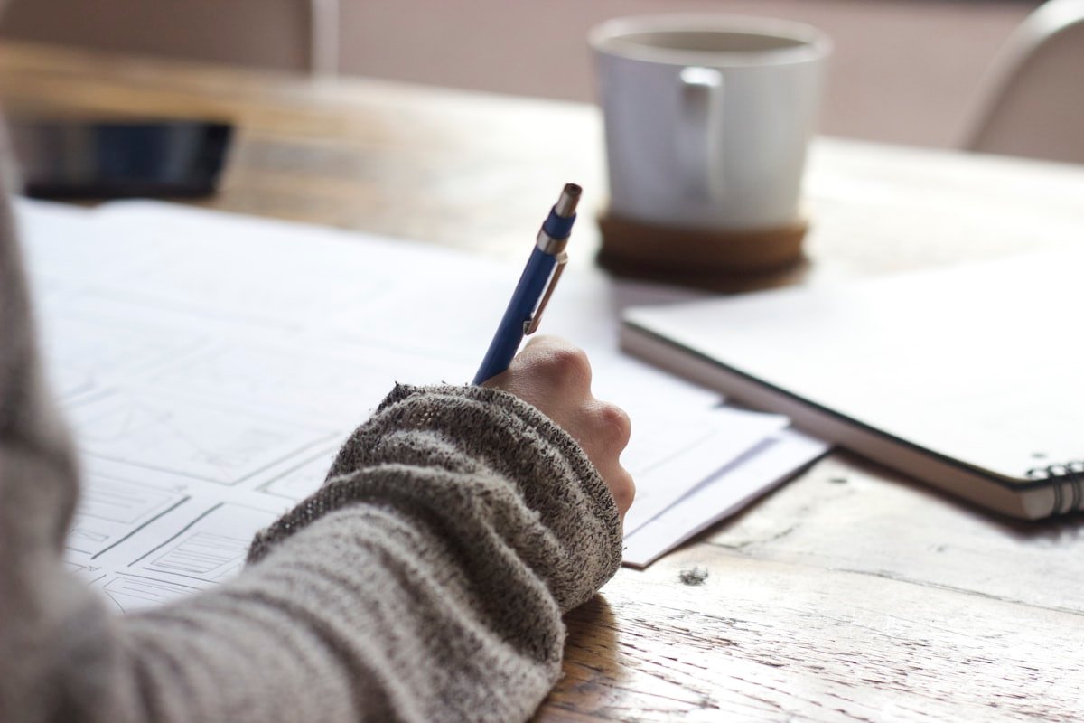 A person writing notes beside a cup of coffee
